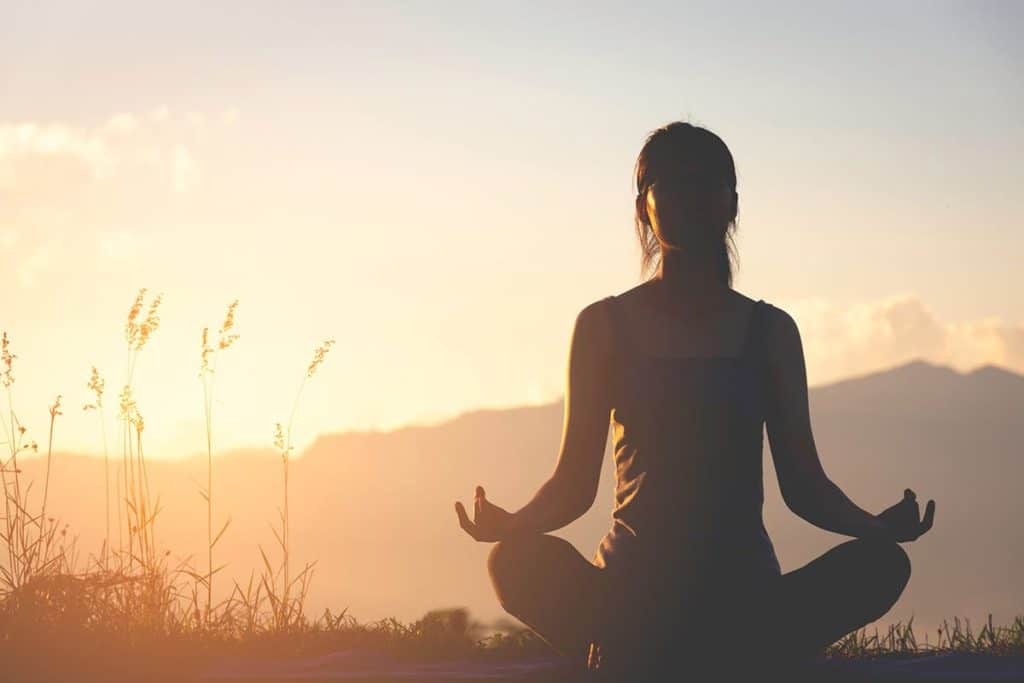 woman sitting in lotus position outside at sunset staring into the distance while engaged in a meditative therapy program in massachusetts