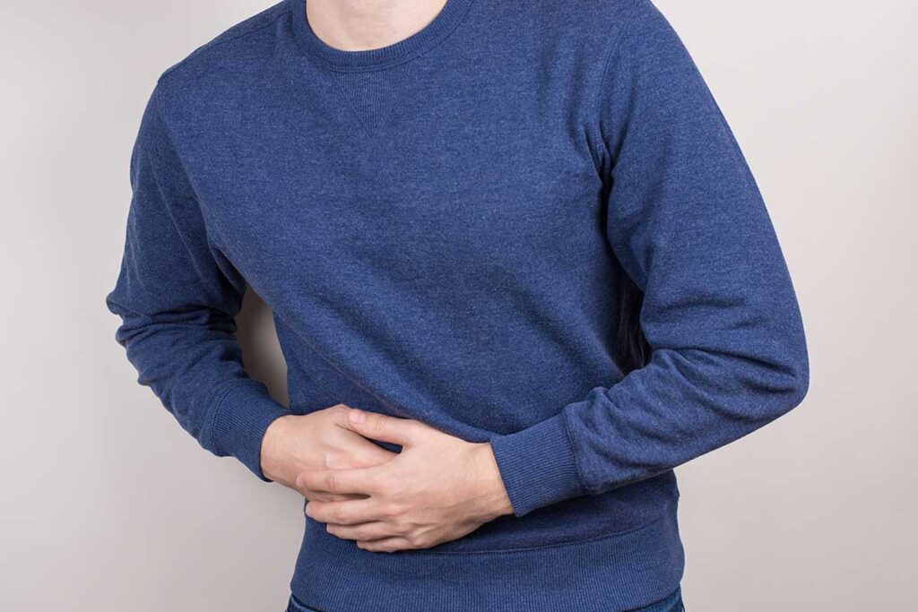 young man holding his abdomen as he experiences the signs of liver damage from alcohol