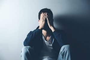 distraught young man sitting with back to a wall in a dimly lit room displaying signs of heroin withdrawal