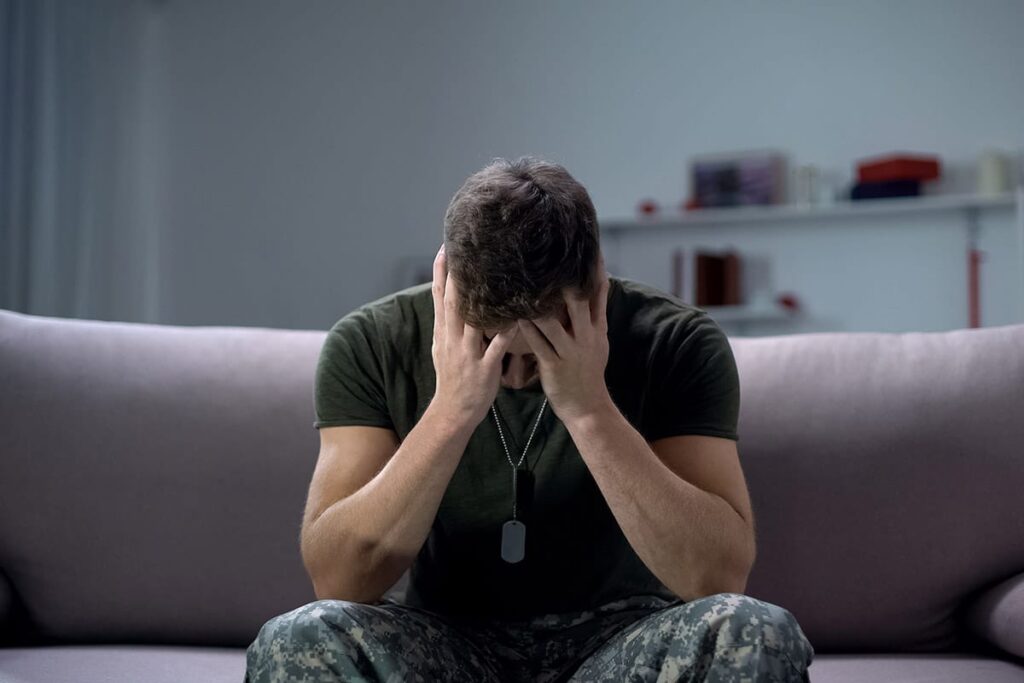veteran sitting on the couch with head in his hands realizing that veterans and substance abuse go hand-in-hand