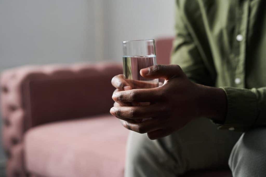 a man sits with a glass of water as he he begins to detox in a drug rehab