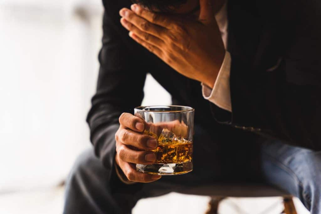 a man sits with a drink in his hand debating whether to continue drinking or admit he should stop