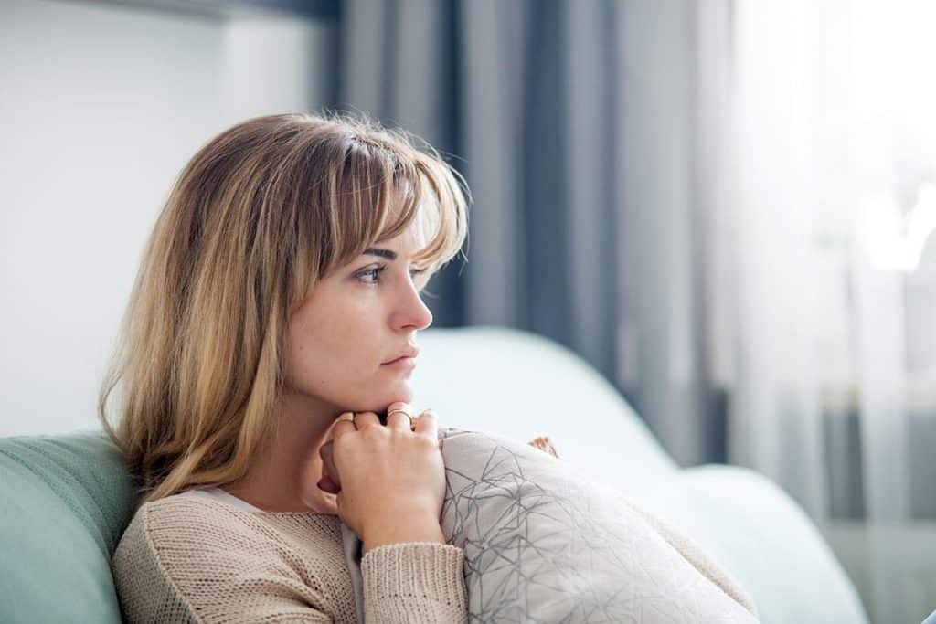 woman sitting alone in room and staring into space as she contemplates the side effects of opioid abuse