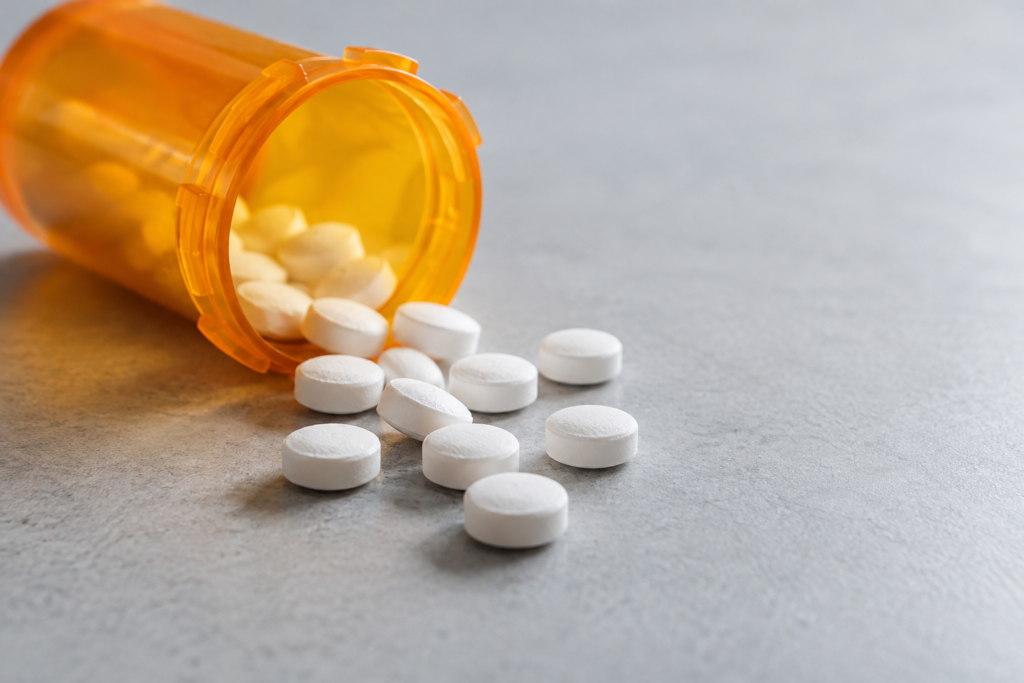 Orange prescription pill bottle tipped over with white tablets spilling onto a gray surface, illustrating the risks of tranq (xylazine) in the drug supply